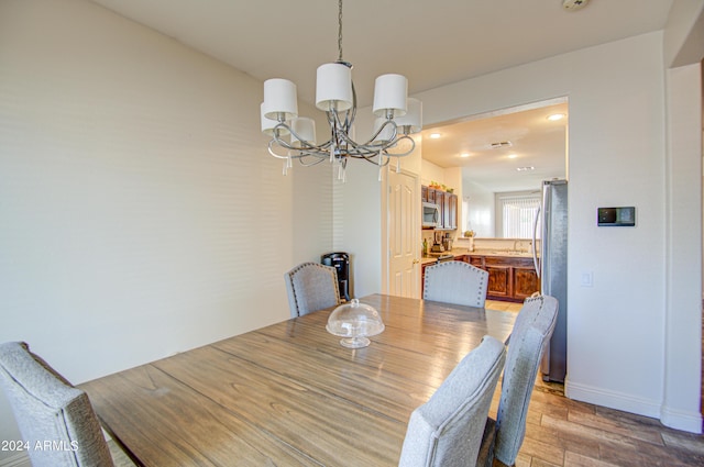 dining space featuring light wood-type flooring, a notable chandelier, and baseboards