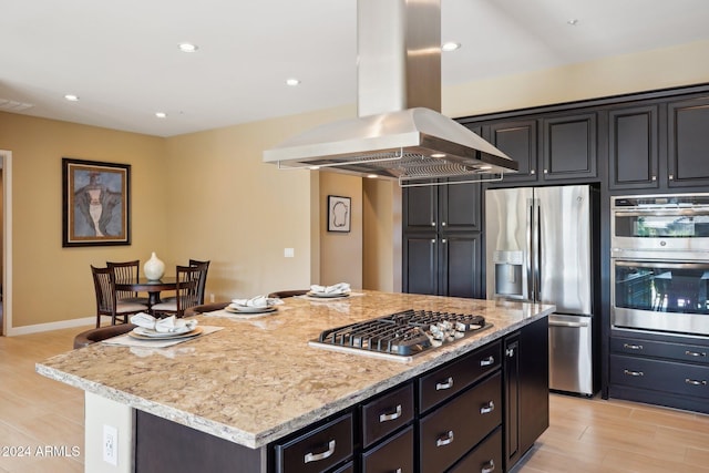 kitchen featuring light stone counters, island range hood, stainless steel appliances, light hardwood / wood-style flooring, and a center island