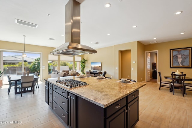 kitchen featuring light stone counters, island range hood, stainless steel gas cooktop, pendant lighting, and a kitchen island