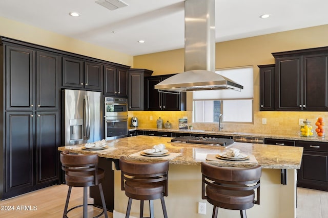 kitchen featuring island exhaust hood, appliances with stainless steel finishes, a center island, and a kitchen breakfast bar