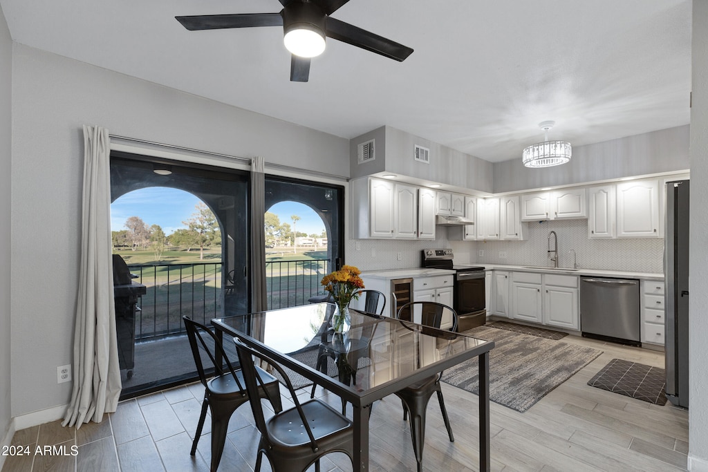 dining room with wine cooler, sink, ceiling fan with notable chandelier, and light hardwood / wood-style flooring