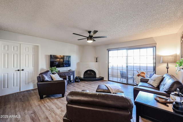 living room featuring wood-type flooring, a textured ceiling, ceiling fan, and a fireplace