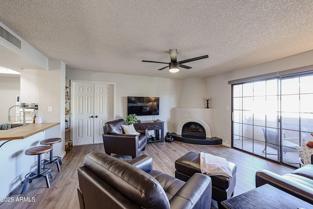 living room with sink, light hardwood / wood-style flooring, a large fireplace, and a textured ceiling