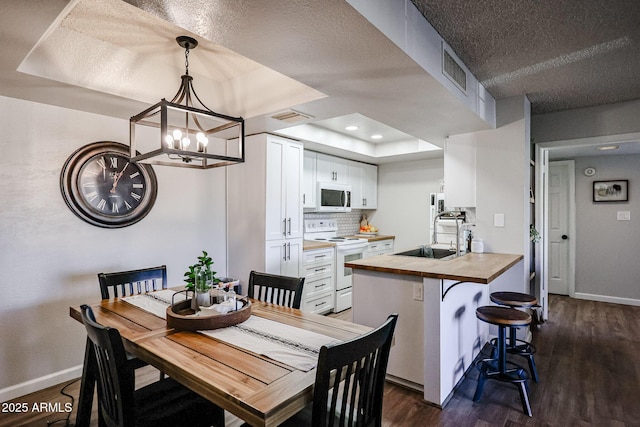 dining area with a textured ceiling, dark hardwood / wood-style flooring, sink, a notable chandelier, and a tray ceiling