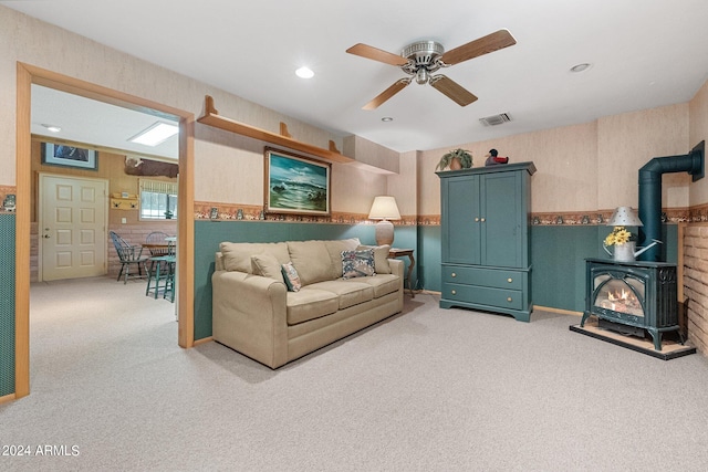 carpeted living room featuring a wood stove and ceiling fan