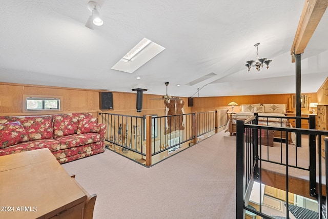 interior space with an inviting chandelier, wooden walls, carpet flooring, and vaulted ceiling with skylight