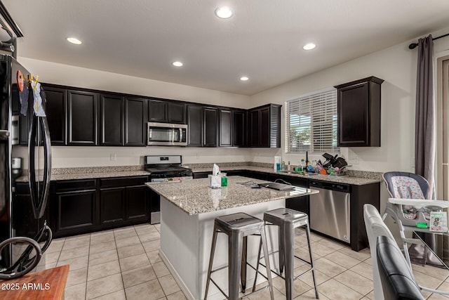 kitchen with a breakfast bar, a center island, light tile patterned floors, light stone counters, and stainless steel appliances