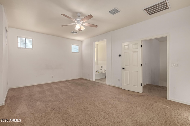 interior space with ceiling fan, multiple windows, light carpet, and ensuite bath