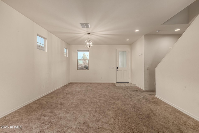 spare room featuring a notable chandelier and light colored carpet