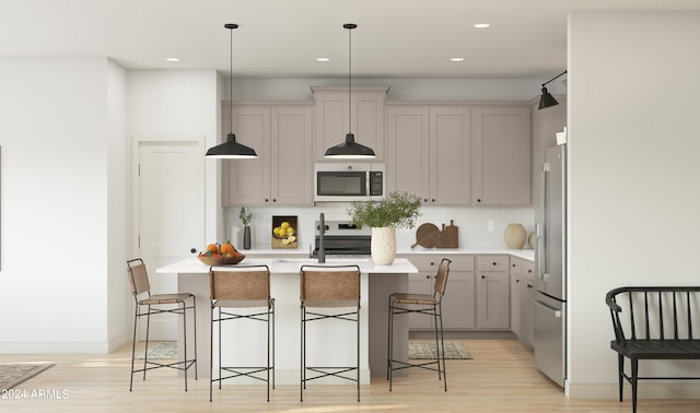 kitchen with pendant lighting, backsplash, appliances with stainless steel finishes, a breakfast bar area, and light wood-type flooring