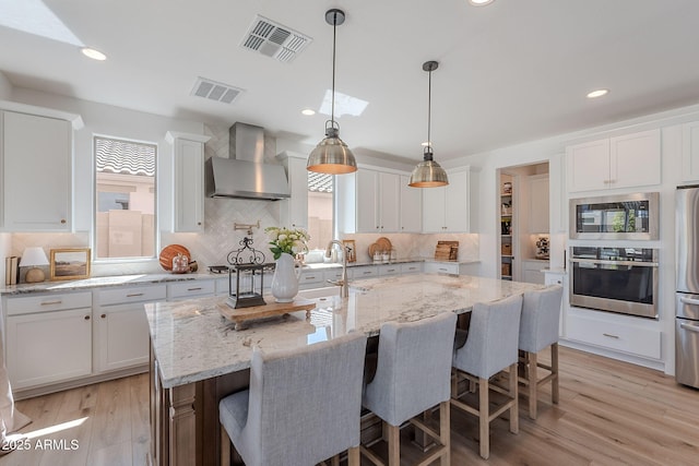 9645 E Ripple Dr, Mesa, AZ 85212 - kitchen featuring stainless steel appliances, wall chimney range hood, white cabinetry, tasteful backsplash, and a kitchen island with sink