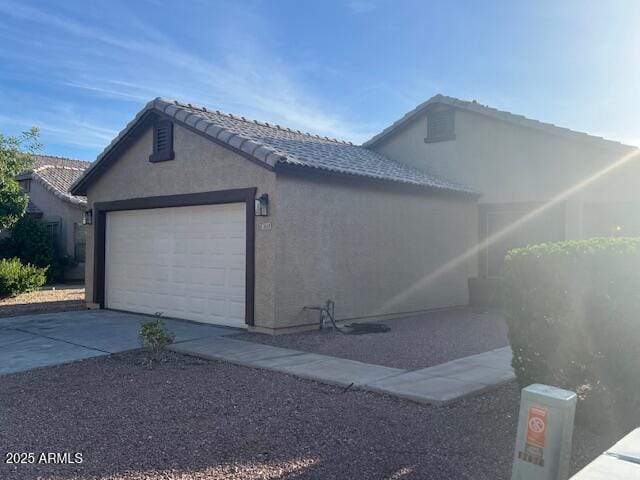 view of home's exterior with a garage, stucco siding, driveway, and a tiled roof