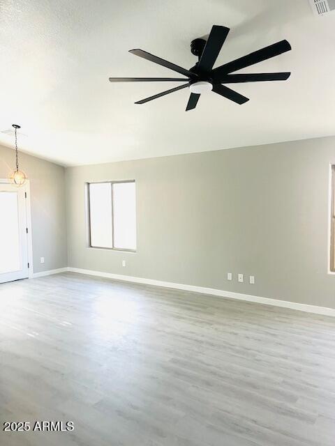 spare room with wood finished floors, a ceiling fan, visible vents, and baseboards