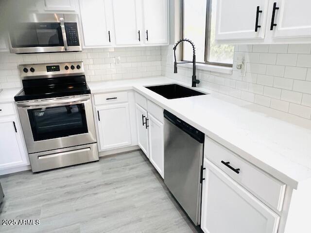 kitchen featuring decorative backsplash, appliances with stainless steel finishes, light countertops, white cabinets, and a sink