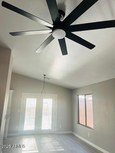 empty room with a textured ceiling, ceiling fan, a wealth of natural light, and french doors