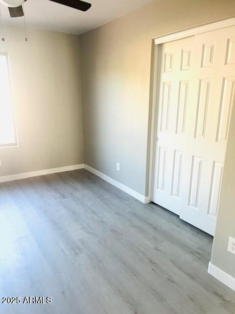 unfurnished bedroom with a closet, ceiling fan, wood finished floors, and baseboards