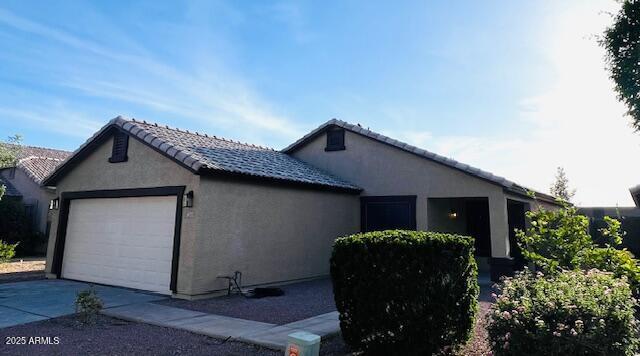 view of side of property with a tile roof, stucco siding, driveway, and an attached garage