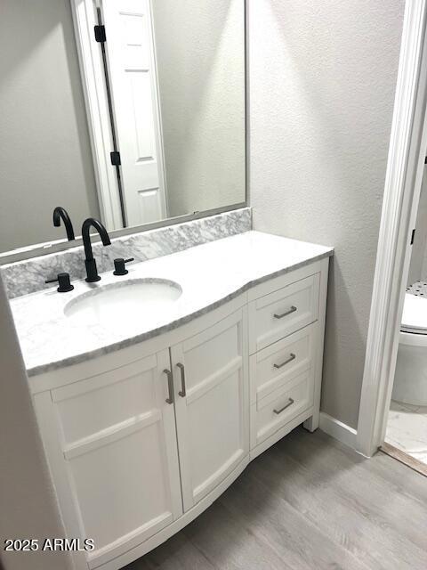 bathroom with toilet, vanity, wood finished floors, and baseboards