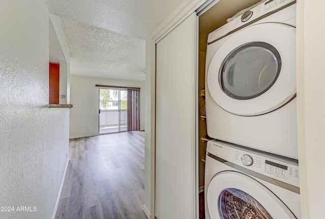 laundry area with a textured ceiling, light hardwood / wood-style floors, and stacked washer / drying machine