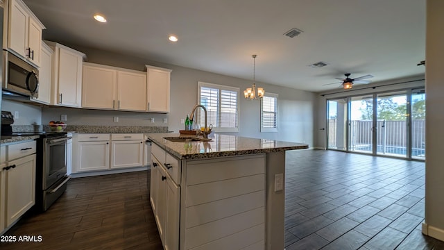 kitchen featuring sink, a kitchen island with sink, light stone countertops, appliances with stainless steel finishes, and ceiling fan with notable chandelier