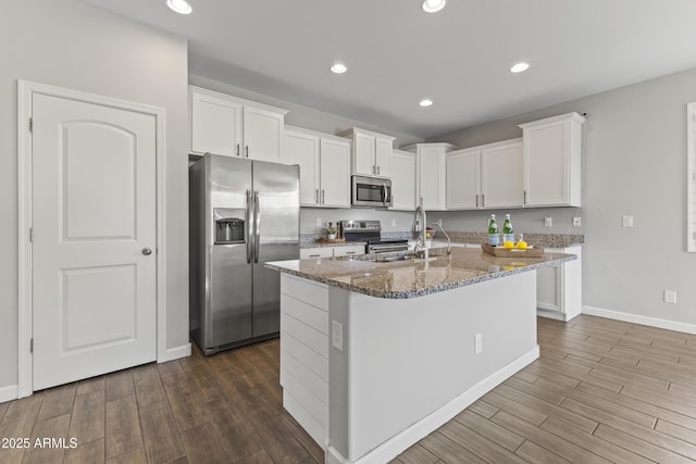 kitchen featuring white cabinetry, a center island with sink, appliances with stainless steel finishes, dark stone countertops, and sink