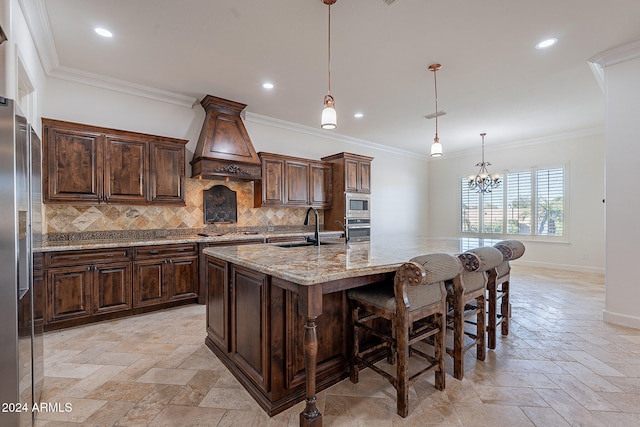 kitchen featuring premium range hood, ornamental molding, a center island with sink, stainless steel appliances, and hanging light fixtures