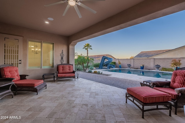 patio terrace at dusk featuring ceiling fan and a fenced in pool