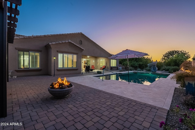 pool at dusk with a patio area and a fire pit