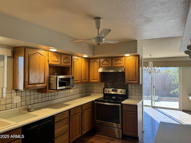 kitchen with brown cabinetry, appliances with stainless steel finishes, light countertops, under cabinet range hood, and backsplash