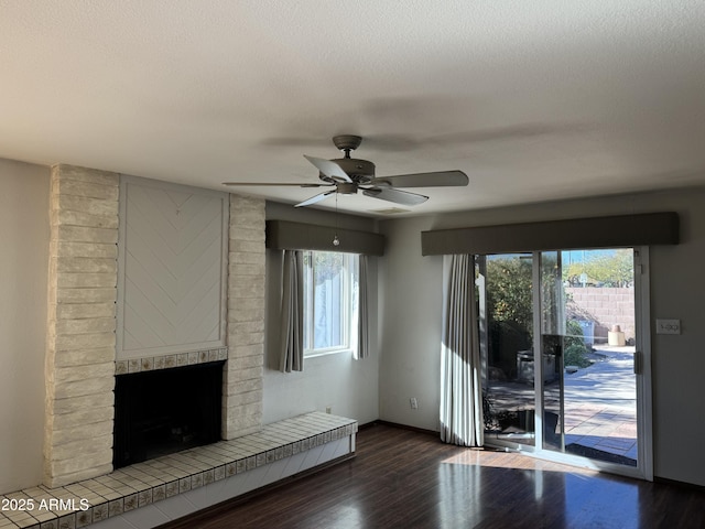 unfurnished living room with ceiling fan, a brick fireplace, a textured ceiling, and dark hardwood / wood-style flooring