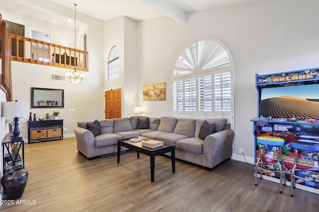 living room featuring beam ceiling, hardwood / wood-style flooring, a chandelier, and a towering ceiling