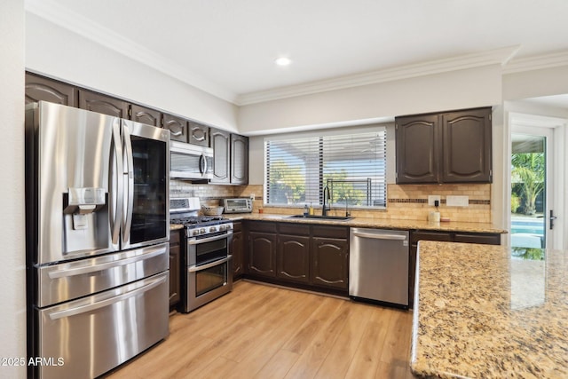 kitchen with appliances with stainless steel finishes, sink, light stone counters, and dark brown cabinets