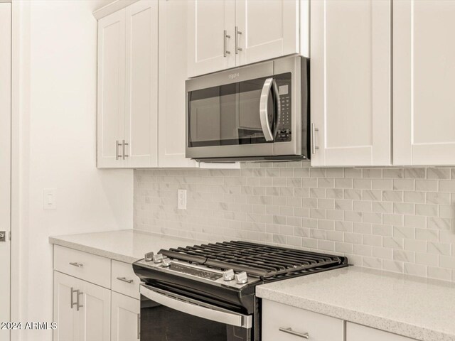 kitchen with white cabinets, decorative backsplash, light stone counters, and stainless steel appliances