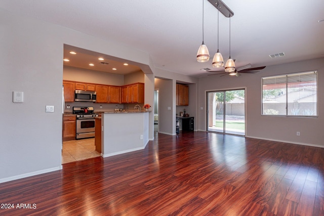 kitchen with ceiling fan, pendant lighting, kitchen peninsula, appliances with stainless steel finishes, and light hardwood / wood-style floors