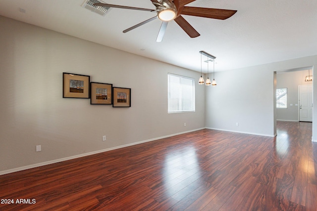 unfurnished room with ceiling fan with notable chandelier, a healthy amount of sunlight, and dark wood-type flooring