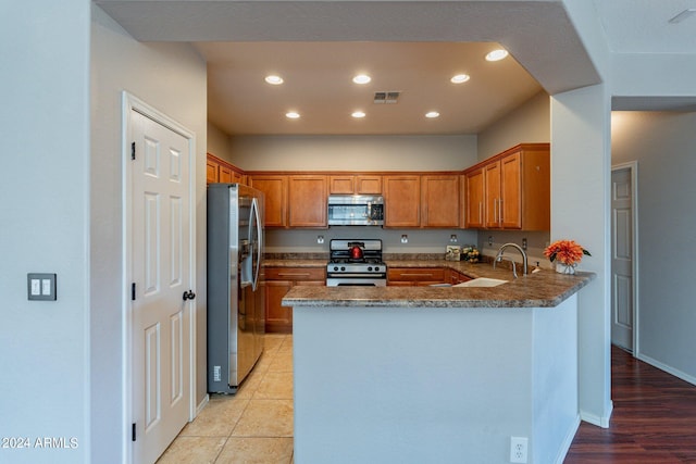 kitchen with sink, kitchen peninsula, light hardwood / wood-style flooring, appliances with stainless steel finishes, and dark stone counters