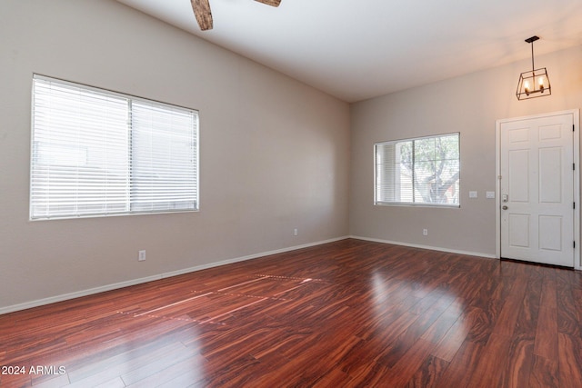 empty room featuring ceiling fan with notable chandelier and dark hardwood / wood-style flooring