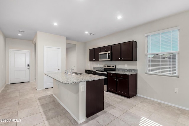 kitchen with sink, light tile patterned floors, dark brown cabinets, a center island with sink, and appliances with stainless steel finishes