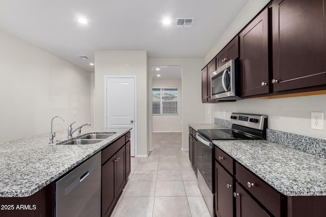 kitchen with sink, a center island with sink, light tile patterned floors, appliances with stainless steel finishes, and dark brown cabinetry