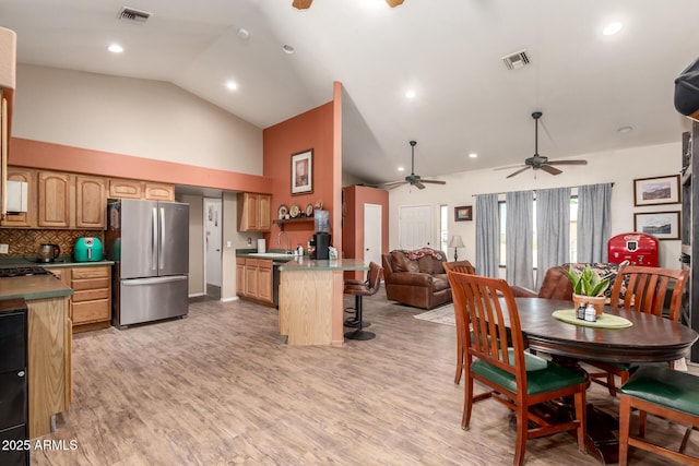 kitchen featuring a peninsula, visible vents, a kitchen breakfast bar, open floor plan, and freestanding refrigerator