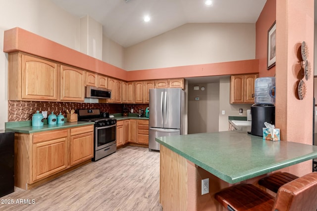 kitchen with a breakfast bar area, stainless steel appliances, tasteful backsplash, light wood-style floors, and a peninsula