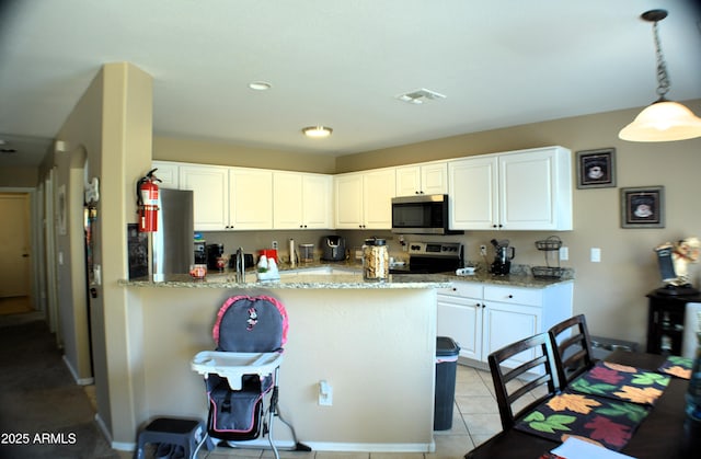 kitchen featuring decorative light fixtures, appliances with stainless steel finishes, light stone countertops, a peninsula, and white cabinetry