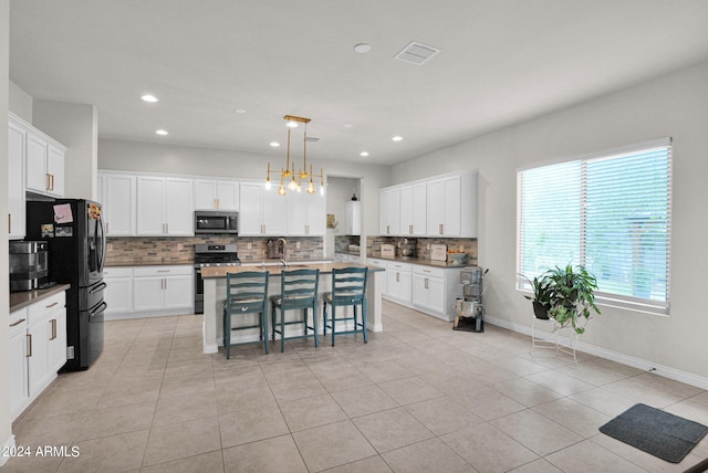 kitchen featuring white cabinets, a kitchen island with sink, stainless steel appliances, and hanging light fixtures