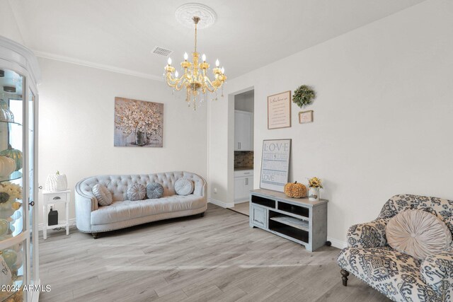 living room with a notable chandelier, light wood-type flooring, and crown molding