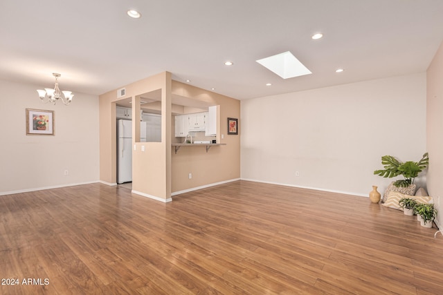 unfurnished living room with hardwood / wood-style floors, a notable chandelier, and a skylight