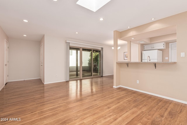 unfurnished living room with light hardwood / wood-style floors and a skylight