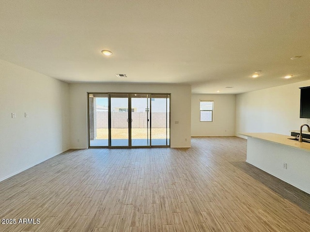 47267 W Mellen Ln, Maricopa, AZ 85139 - unfurnished living room with light wood-style floors, recessed lighting, a sink, and baseboards