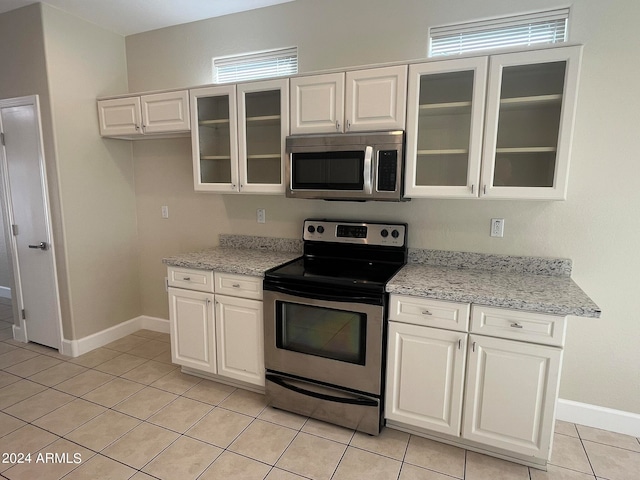 kitchen with light tile patterned flooring, white cabinetry, stainless steel appliances, and light stone counters