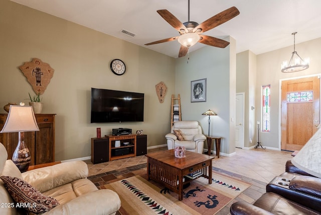living area with visible vents, baseboards, ceiling fan with notable chandelier, and a high ceiling
