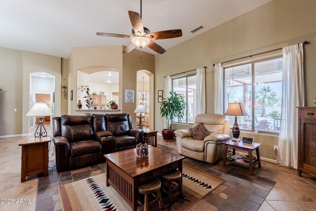 living room with arched walkways, a ceiling fan, baseboards, visible vents, and stone tile flooring